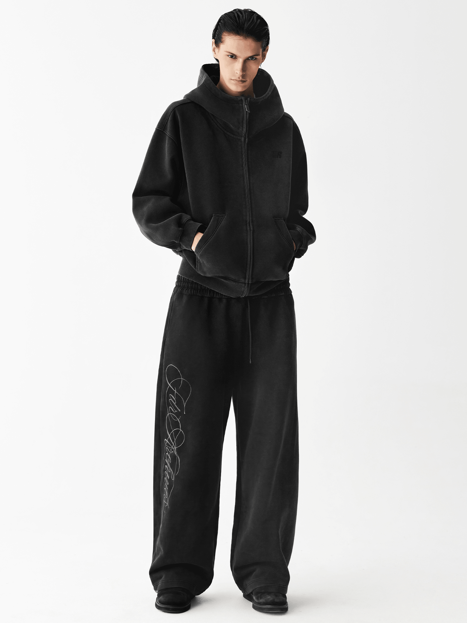 Full body shot of a male model wearing an oversized black zip-up hoodie and matching wide-leg sweatpants