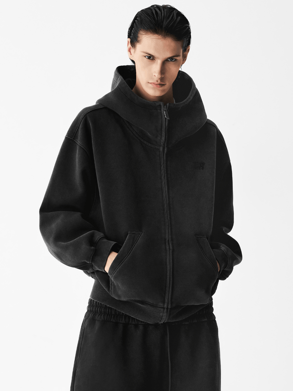 Close-up of a male model wearing a black zip-up hoodie with hands in pockets.