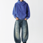 Full body shot of a male model wearing a royal blue zip-up hoodie with baggy jeans.