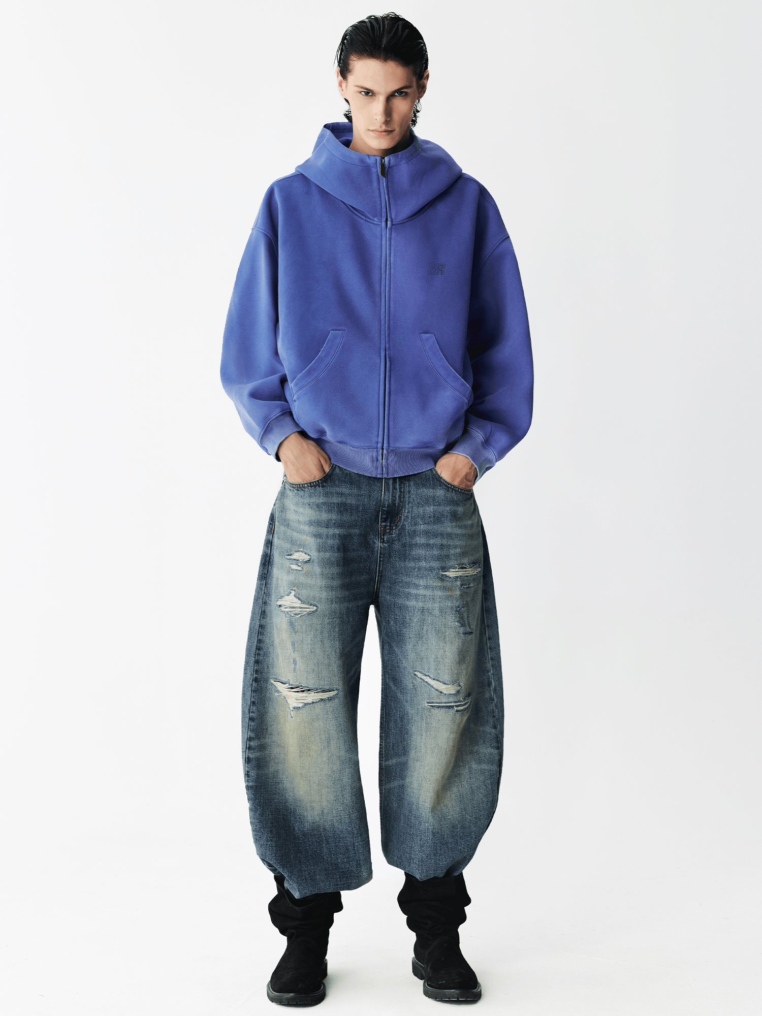 Full body shot of a male model wearing a royal blue zip-up hoodie with baggy jeans.