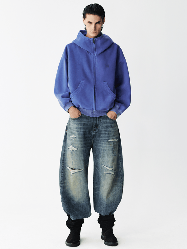Full body shot of a male model wearing a royal blue zip-up hoodie with baggy jeans.