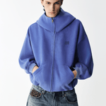 Half-body shot of a male model wearing a royal blue high-neck zip-up hoodie.