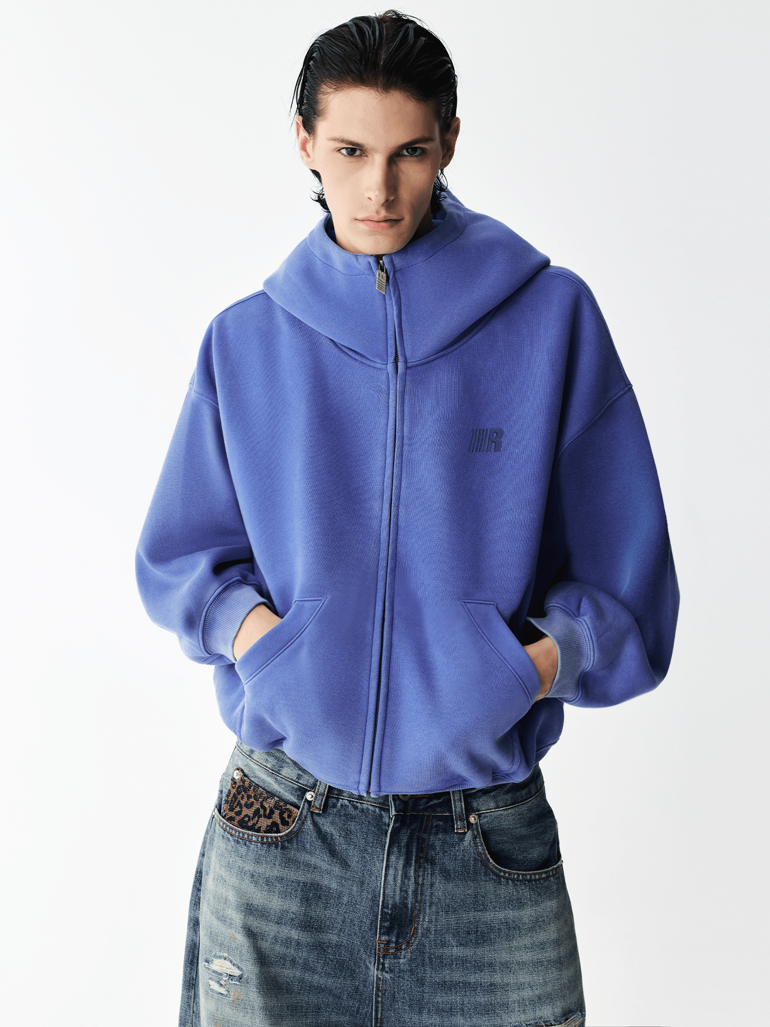Half-body shot of a male model wearing a royal blue high-neck zip-up hoodie.