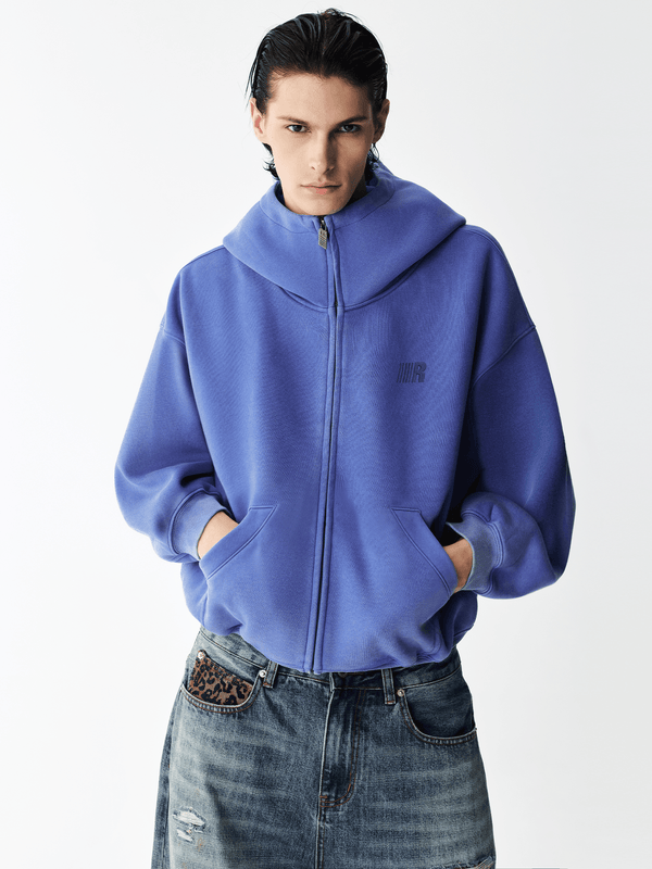 Half-body shot of a male model wearing a royal blue high-neck zip-up hoodie.