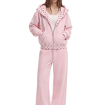 A model wearing a light pink two-piece tracksuit with a hooded zip-up jacket and matching wide-leg pants. The jacket features a white inner hood lining with pink polka dots and a matching polka-dot patterned zipper trim.