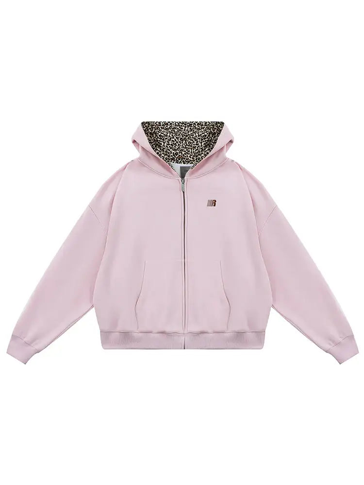 Flat lay of pink cropped zip-up hoodie with leopard print lined hood and cat ears, pastel edgy fashion.