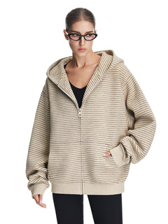 A model wearing an oversized cream-colored textured zip-up hoodie with a structured hood and drop shoulders, styled for a modern lifestyle aesthetic.