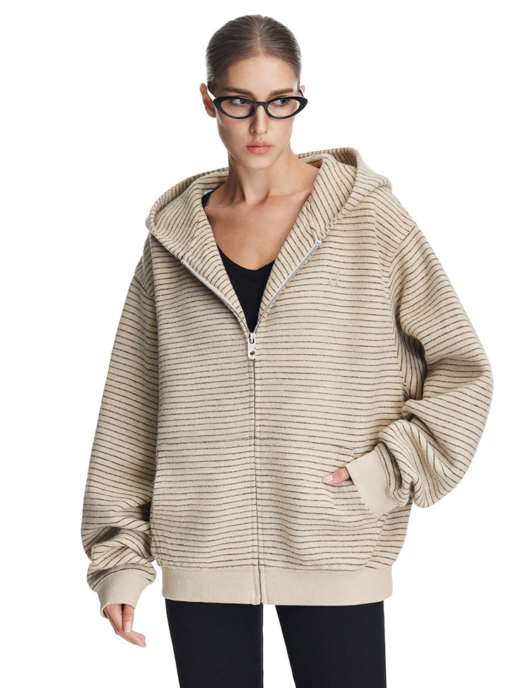A model wearing an oversized cream-colored textured zip-up hoodie with a structured hood and drop shoulders, styled for a modern lifestyle aesthetic.