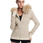 A model wearing a cream-colored, ribbed-knit hooded jacket with a brown faux fur-trimmed hood and black tank top underneath, posed against a white background.