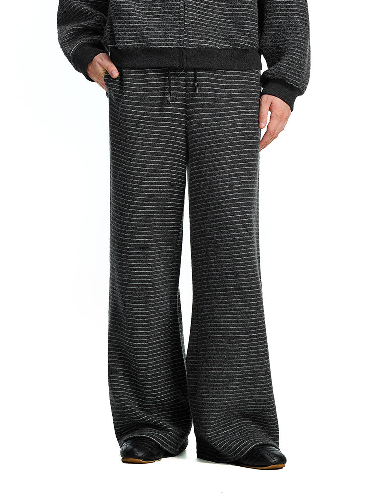 A model wearing charcoal black wide-leg textured pants paired with a matching dark sweatshirt, showcasing a coordinated monochrome lifestyle look.