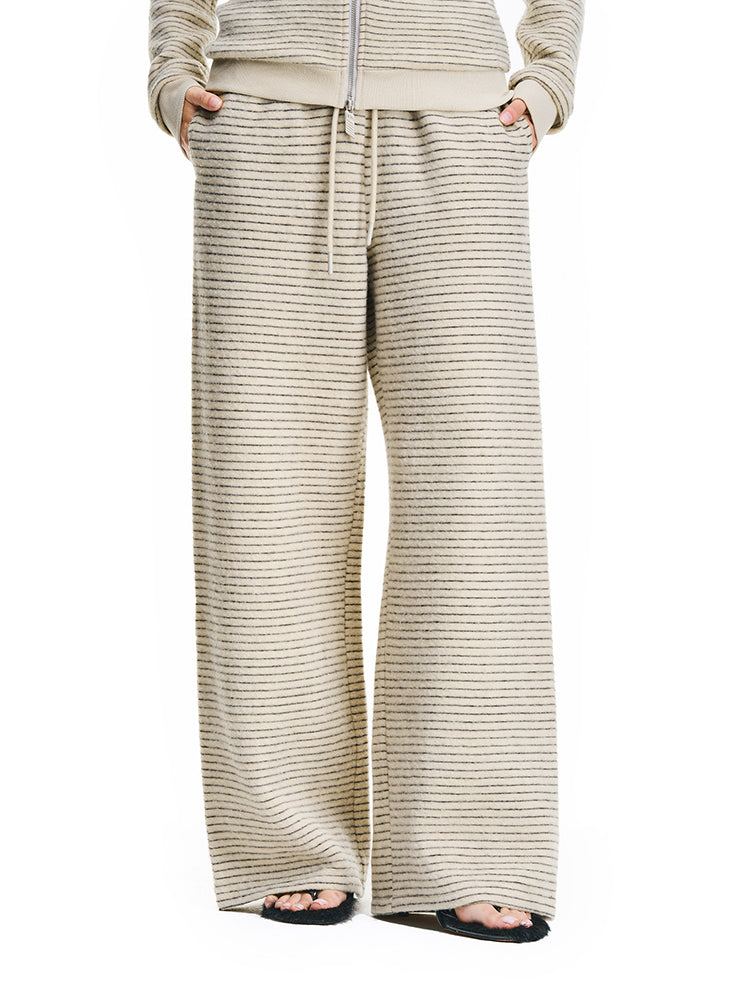 A front view of a model wearing cream-colored, wide-leg textured lounge pants with a matching zip-up hoodie, featuring a relaxed fit and drawstring waist.