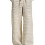 A front view of a model wearing cream-colored, wide-leg textured lounge pants with a matching zip-up hoodie, featuring a relaxed fit and drawstring waist.