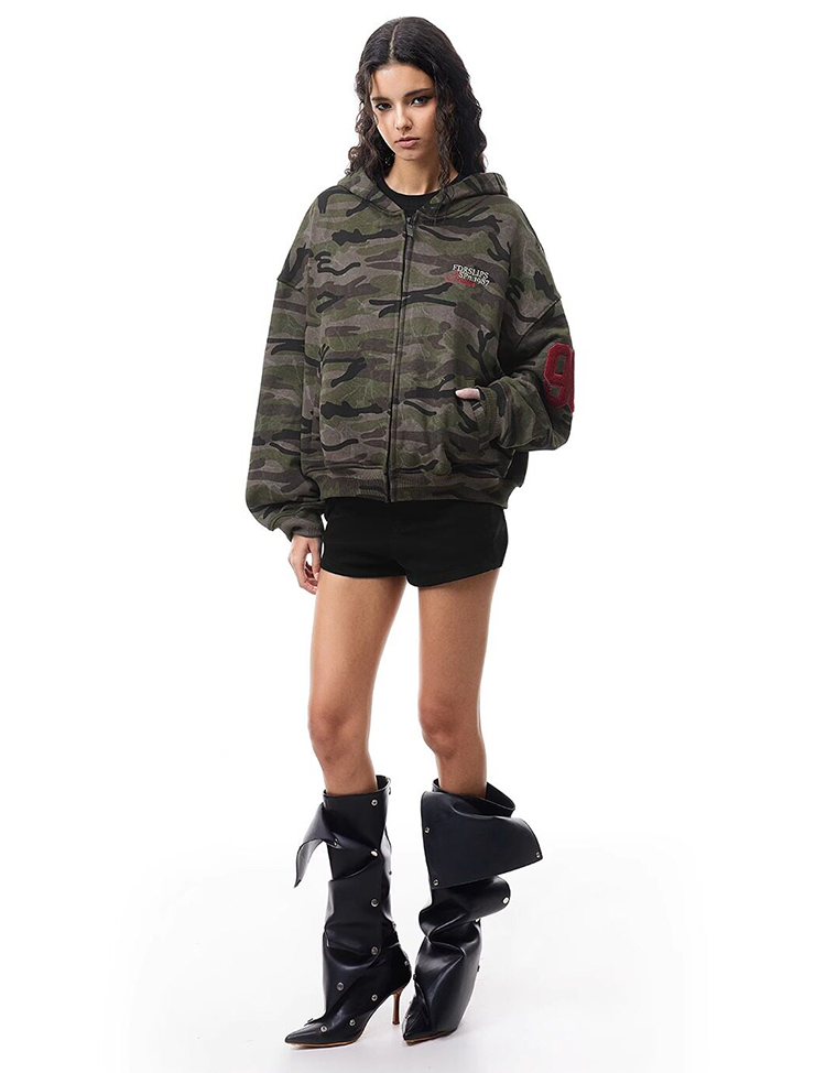 Full body shot of model in dark camo hoodie with oversized boots, high-street Y2K fashion aesthetic.