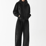 Full body shot of a male model wearing an oversized washed black embroidered zip hoodie and matching wide-leg pants.