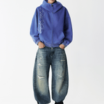 Full body shot of a male model wearing a washed blue embroidered zip hoodie with wide-leg distressed jeans.