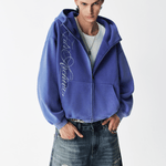Medium shot of a male model in an open washed blue embroidered zip hoodie over a gray t-shirt.