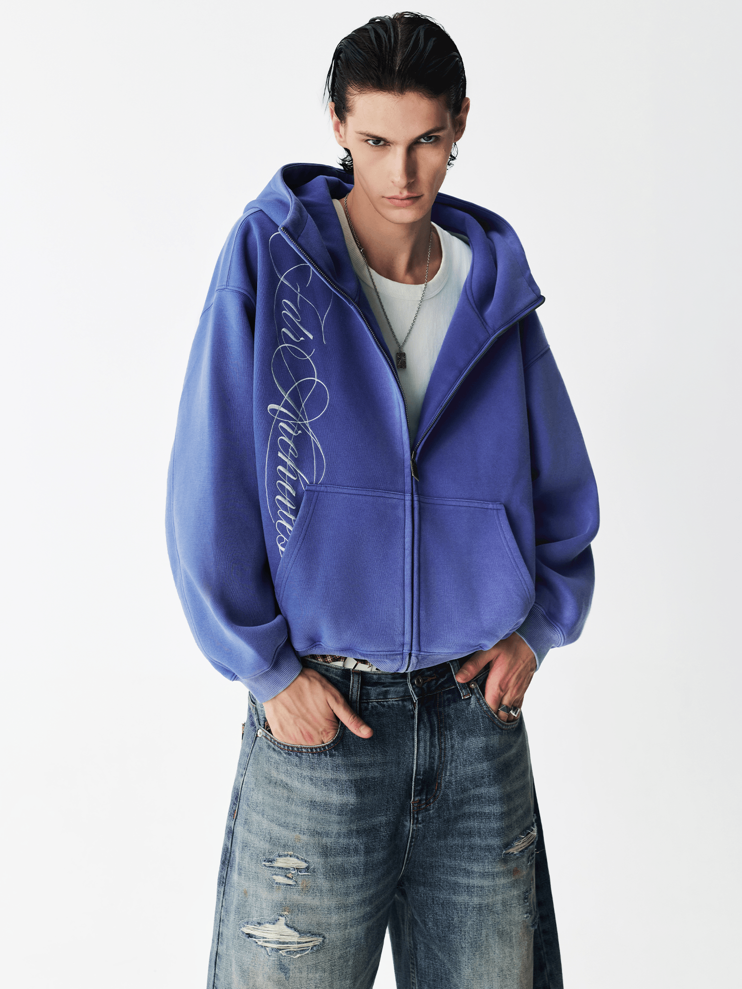 Medium shot of a male model in an open washed blue embroidered zip hoodie over a gray t-shirt.