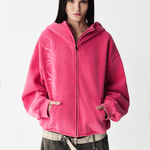 Front half-body view of a female model wearing a washed pink embroidered zip-up hoodie.