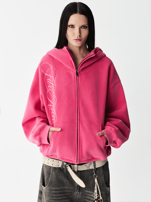 Front half-body view of a female model wearing a washed pink embroidered zip-up hoodie.