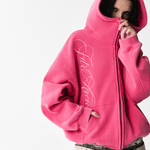 Close-up of a female model wearing a washed pink hoodie with the hood pulled up covering the lower face.