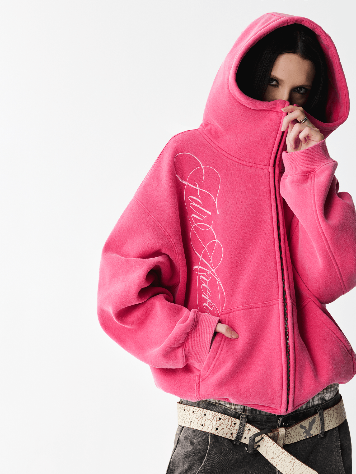 Close-up of a female model wearing a washed pink hoodie with the hood pulled up covering the lower face.