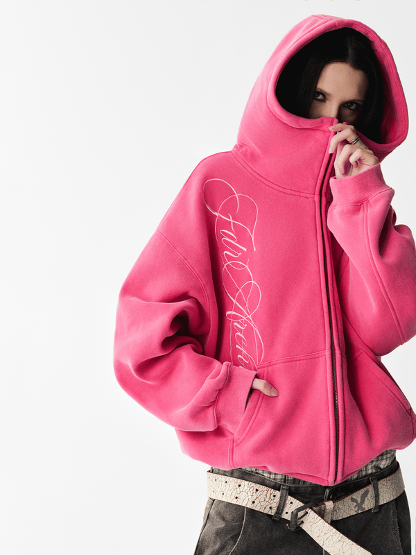 Close-up of a female model wearing a washed pink hoodie with the hood pulled up covering the lower face.