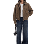 Person wearing a brown jacket with fur trim and dark jeans on a white background