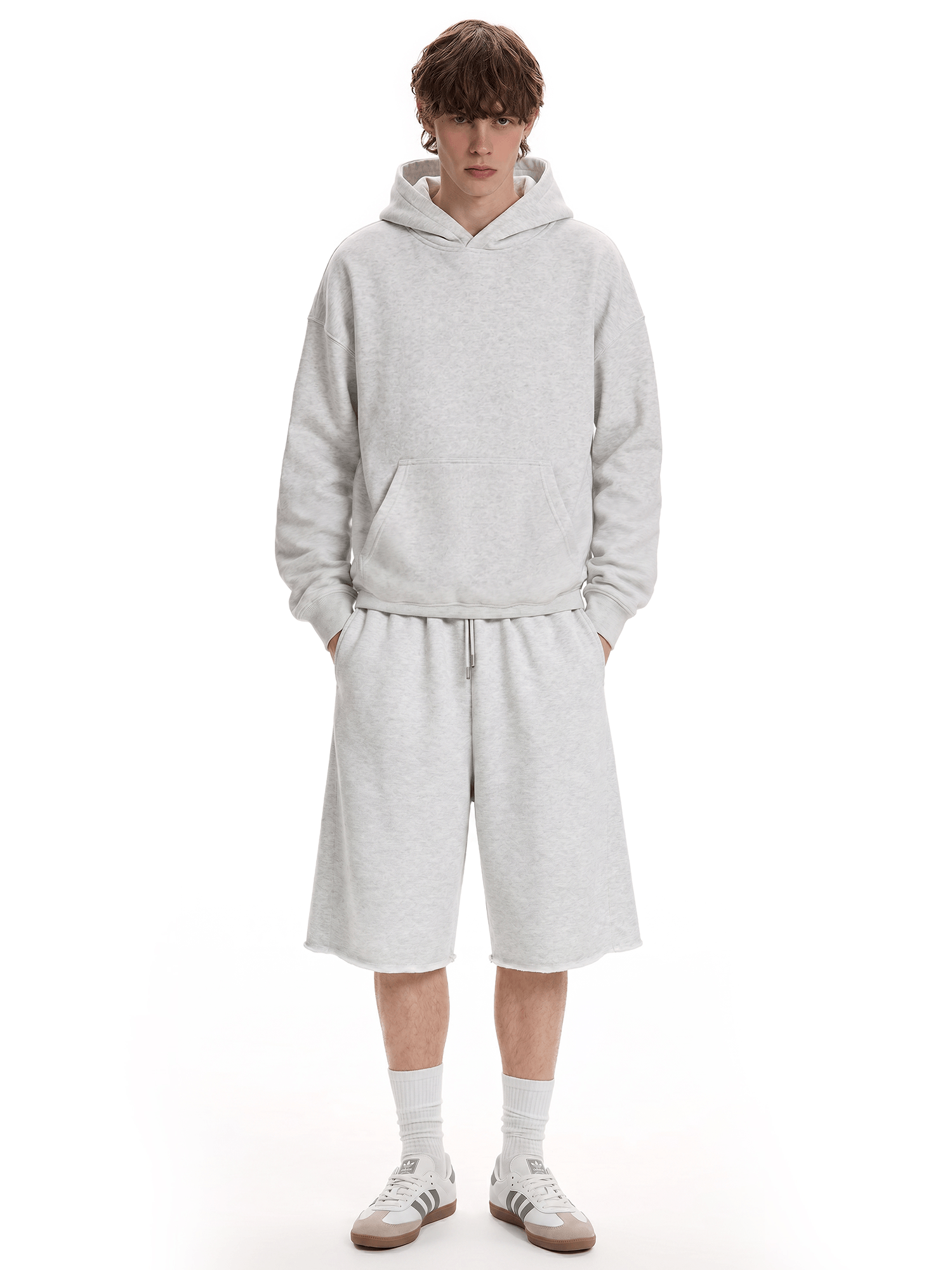 Full-body front view of a model wearing a light gray hoodie and matching shorts, paired with white socks and light-colored sneakers.