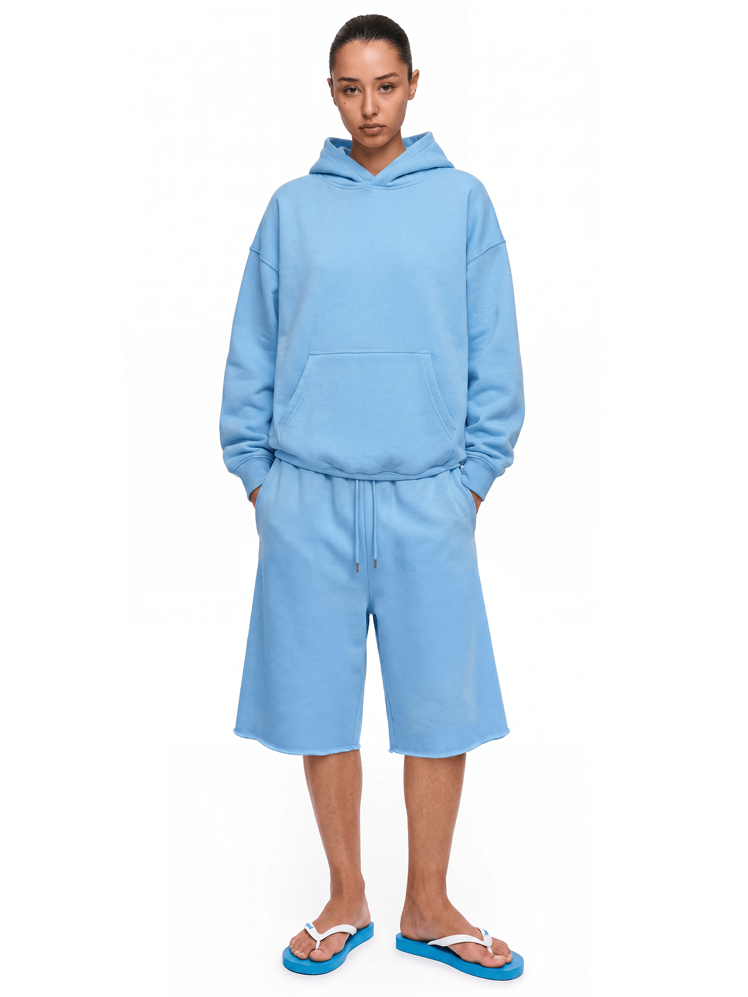 Full-body front view of a model wearing a lake blue hoodie and matching shorts, paired with blue flip-flops.