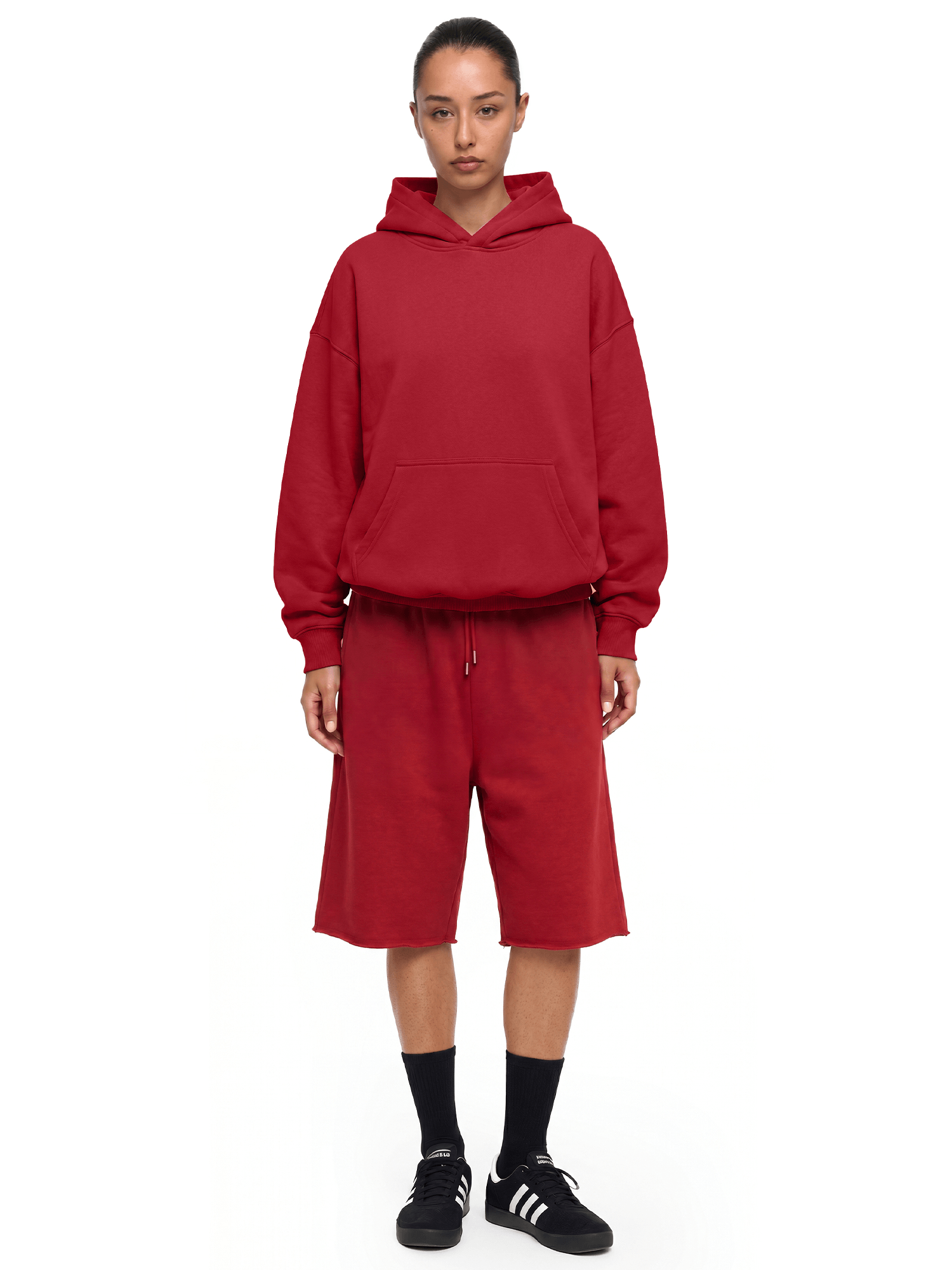 Full-body front view of a model wearing a dark red hoodie and matching shorts, paired with black socks and black shoes.