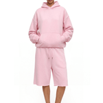 Full-body front view of a model wearing a light pink hoodie and matching loose over-the-knee shorts, paired with pink sandals.