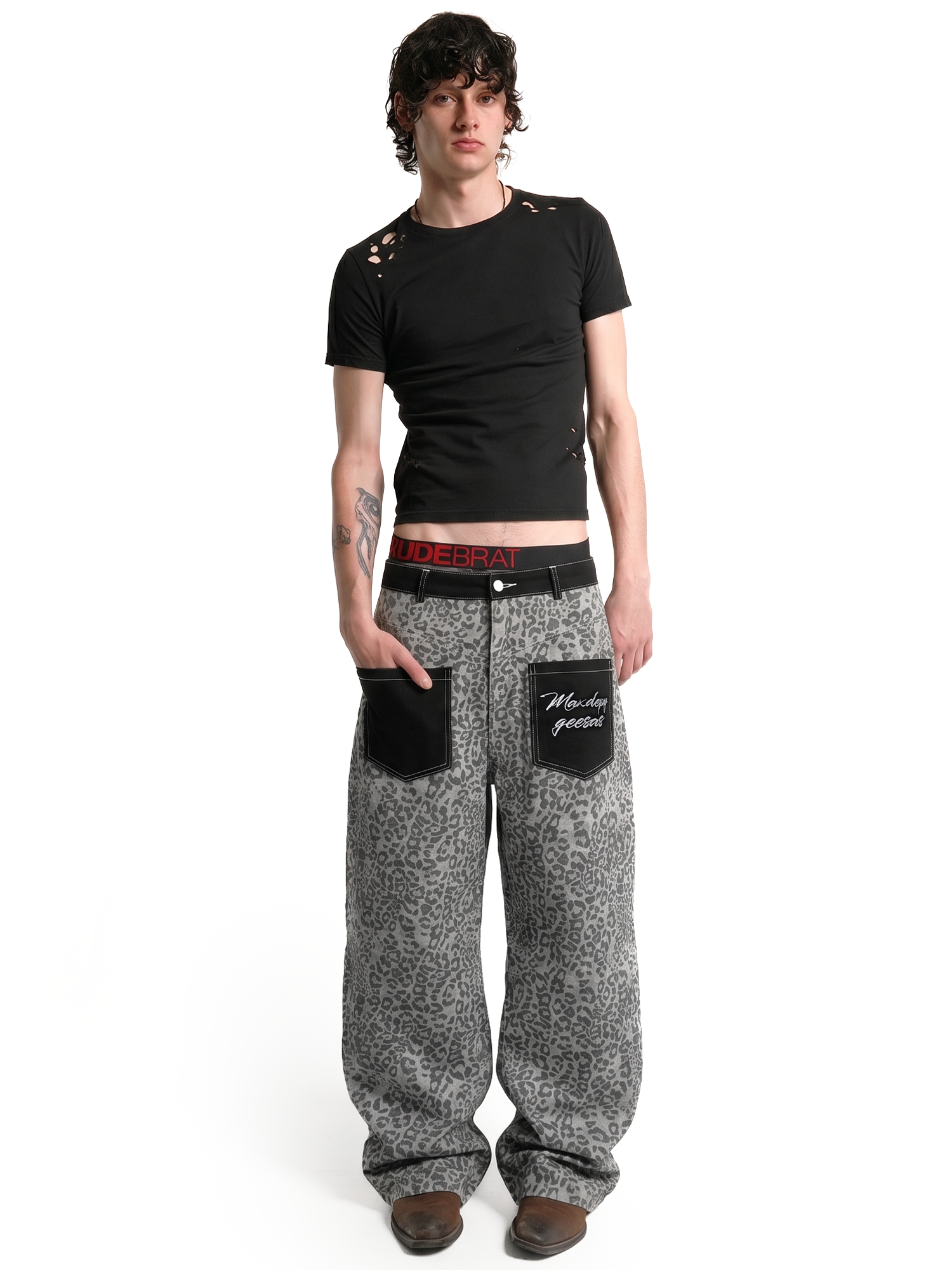 Full-body front view of a male model wearing grey leopard print wide-leg trousers and a black t-shirt for a street-style look.