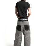 Back view of a male model showcasing the loose fit and black contrast back pockets of the grey leopard print pants.