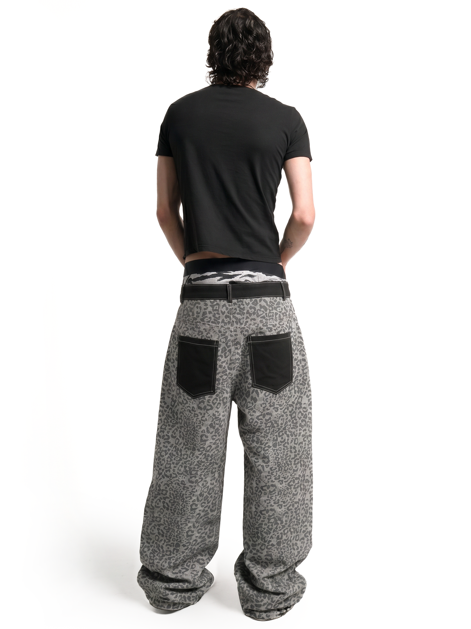 Back view of a male model showcasing the loose fit and black contrast back pockets of the grey leopard print pants.