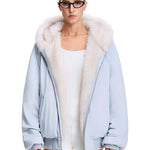 Vollständige Vorderansicht eines Modells, das eine helle pastellblaue Kapuzenjacke mit weißer Kunstfellbesatz trägt und deren Passform gezeigt wird