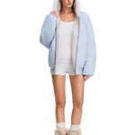 Ganzkörperaufnahme einer Modelin, die in einer hellblauen Damen-Felljacke mit Kapuze posiert und bei der die weiße Borte hervorgehoben wird