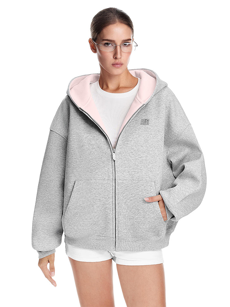 Detail shot of a grey boxy hoodie with pink contrast lining and hand in pocket, relaxed urban fit.