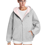 Detail shot of a grey boxy hoodie with pink contrast lining and hand in pocket, relaxed urban fit.