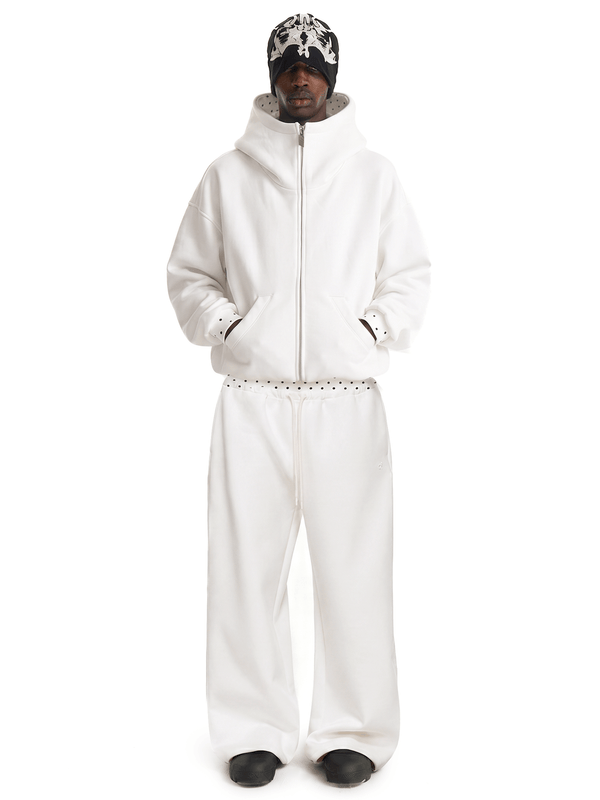 Vue de face en corps entier d'un mannequin masculin posant dans un survêtement style cyber y2k baggy en blanc cassé, avec un sweat à capuche zippé oversize et un pantalon de survêtement ample.