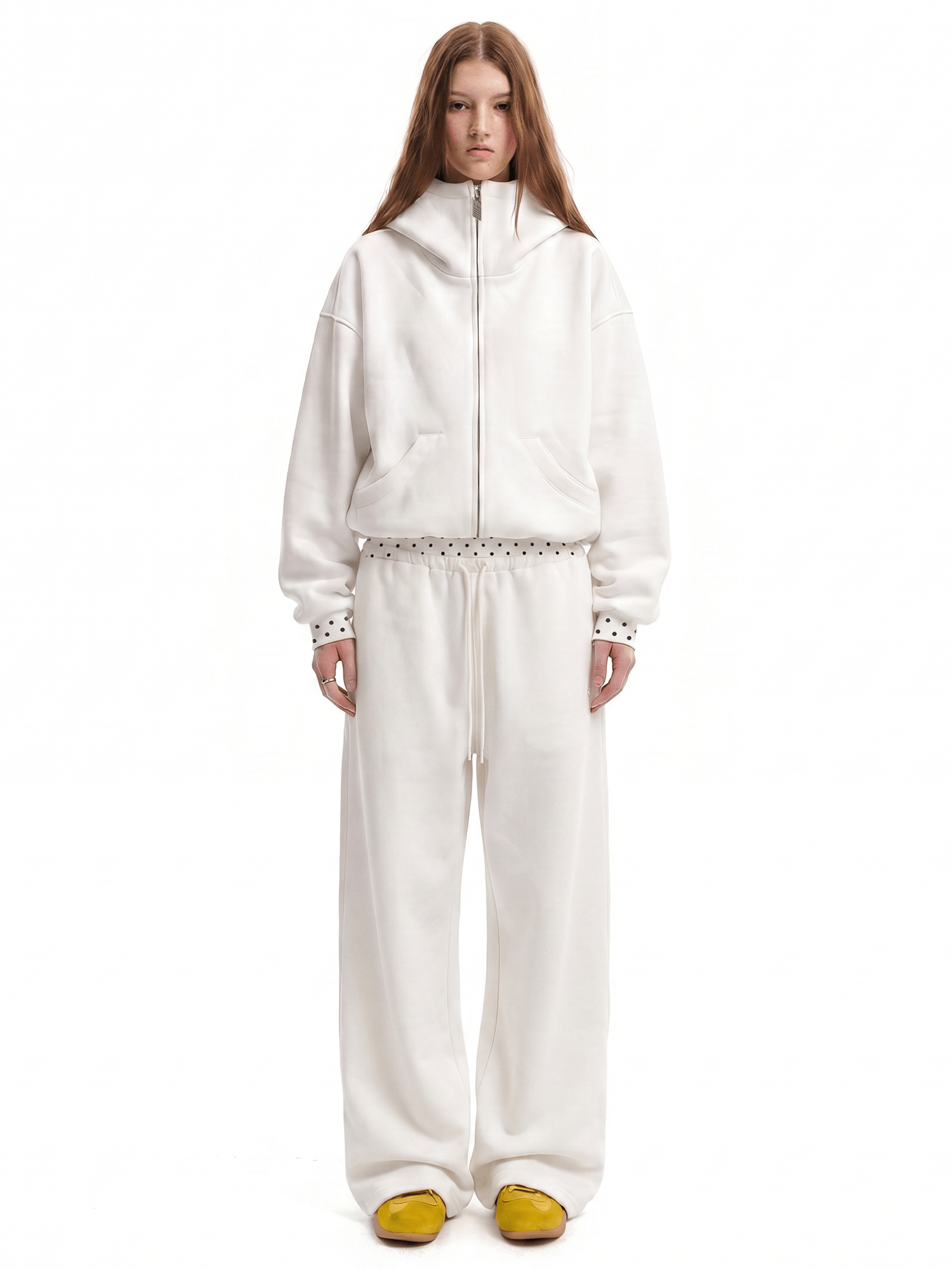 Full-length shot of a model styling an off-white unisex baggy streetwear tracksuit with vibrant yellow shoes, clean aesthetic techwear vibes.