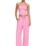 Woman wearing a pink strapless top and wide-leg pants on a white background