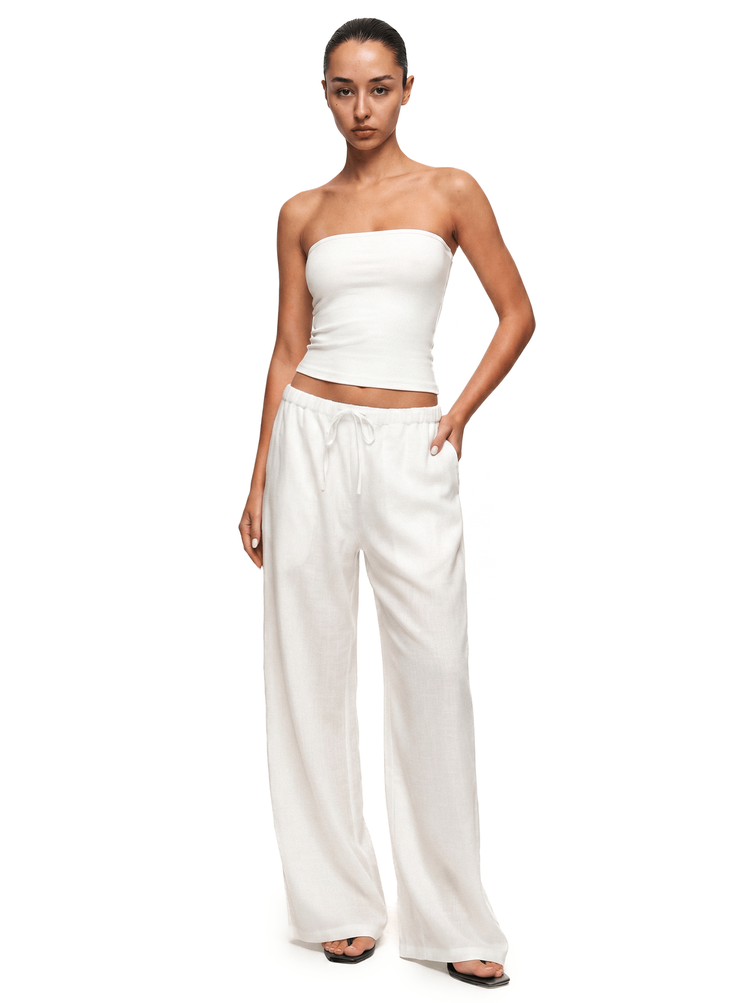 Woman wearing a white strapless top and wide-leg pants on a white background