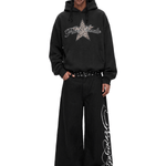 Model wearing a black oversized Y2K star graphic hoodie and matching black wide-leg baggy streetwear jeans, full body studio shot.
