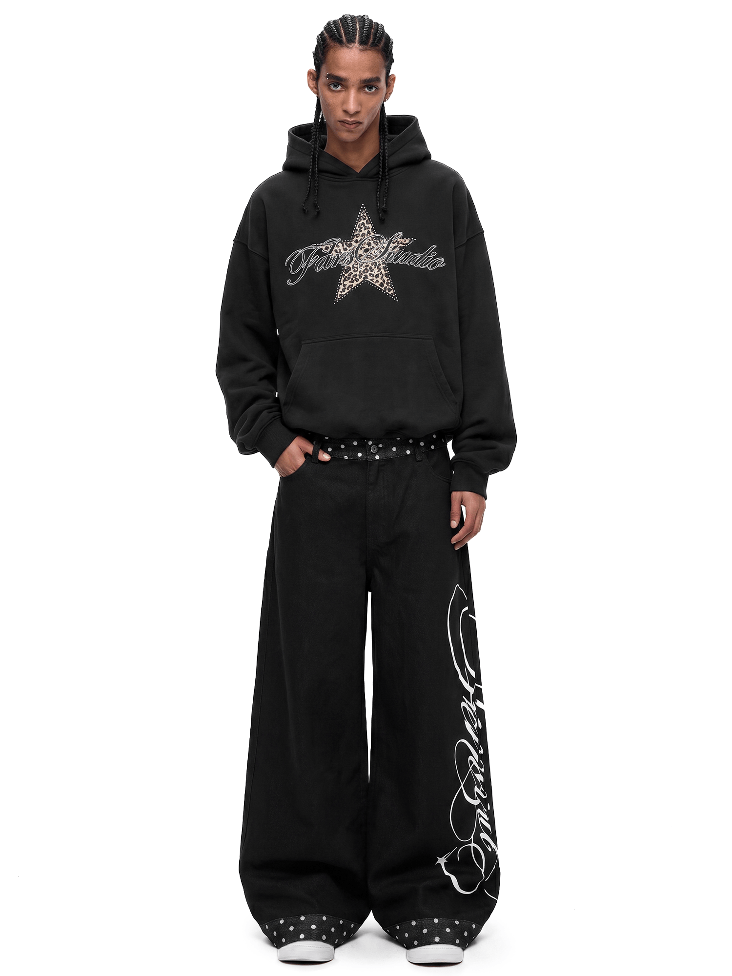 Model wearing a black oversized Y2K star graphic hoodie and matching black wide-leg baggy streetwear jeans, full body studio shot.