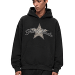 Close-up shot of a black streetwear hoodie featuring a distressed star graphic on the chest with a model posing.