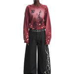 Full-length shot of a model wearing a distressed red gradient long-sleeve tee and oversized black embroidered wide-leg trousers.