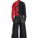 Rear view of a model in a red and black color-block sweatshirt and baggy black streetwear pants with leg embroidery.