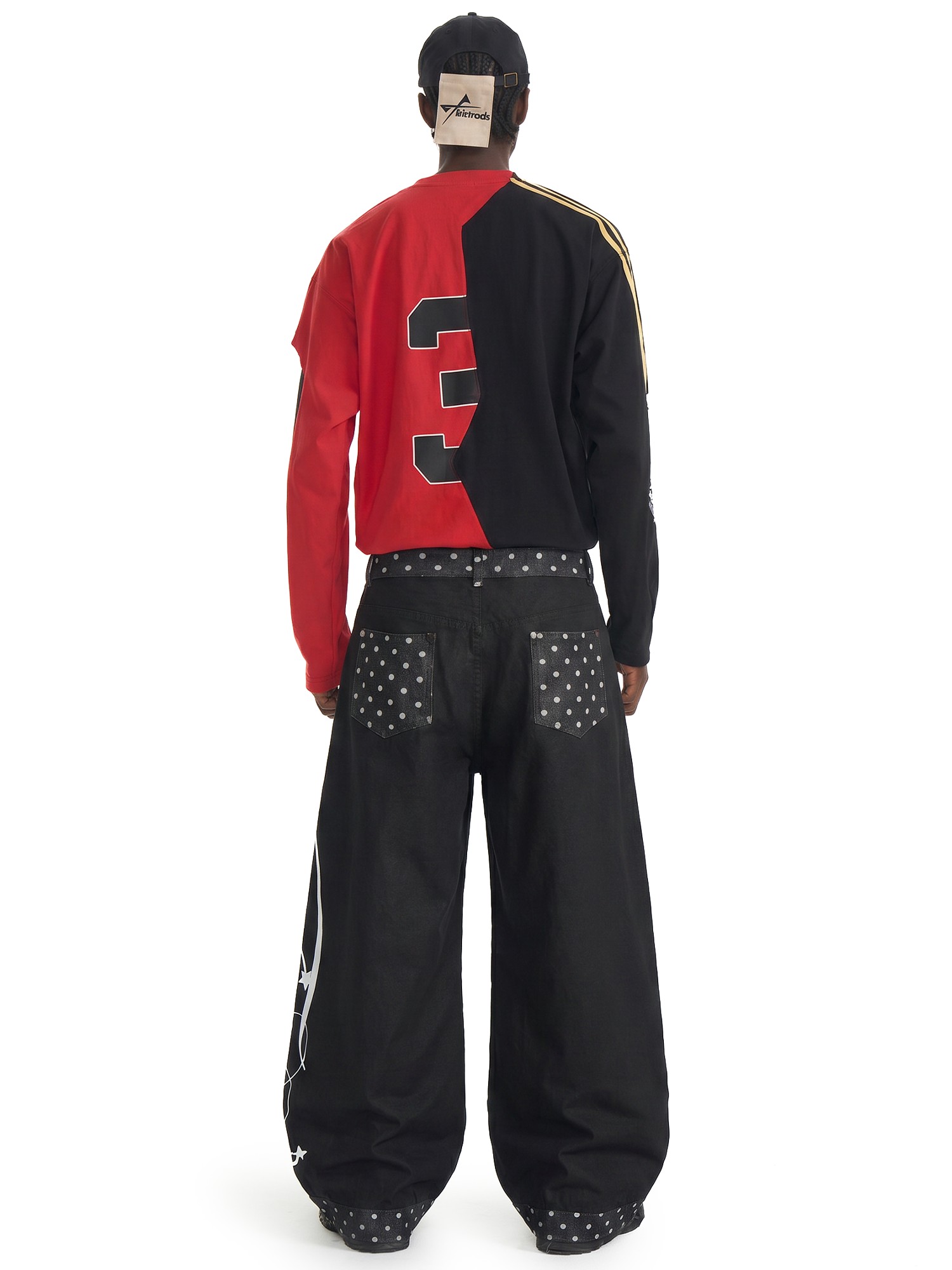Rear view of a model in a red and black color-block sweatshirt and baggy black streetwear pants with leg embroidery.