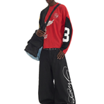 Side profile of a model carrying a black crossbody bag, wearing oversized black cargo pants with white script embroidery.