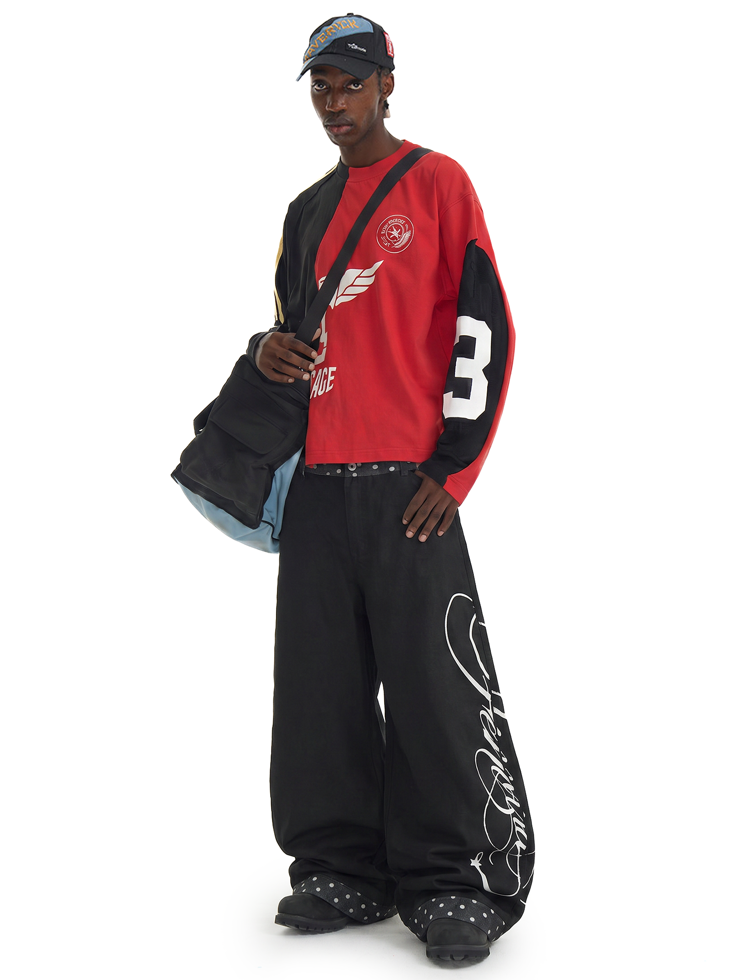 Profil de côté d'un mannequin portant un sac bandoulière noir, vêtu d'un pantalon cargo noir oversize avec une broderie en script blanc